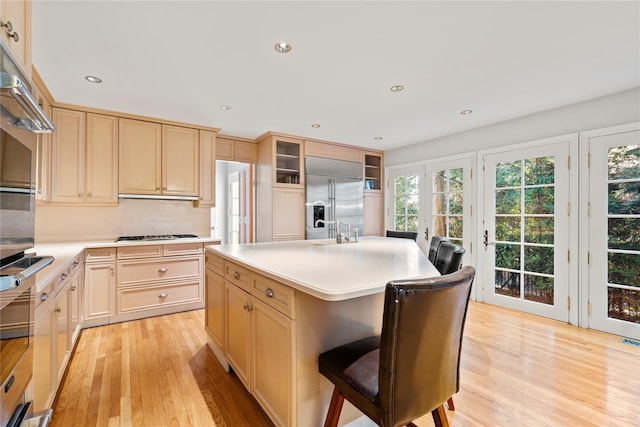 kitchen featuring a kitchen island with sink, light hardwood / wood-style flooring, light brown cabinets, and appliances with stainless steel finishes