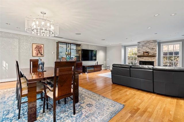 dining space with a stone fireplace, ornamental molding, and light wood-type flooring