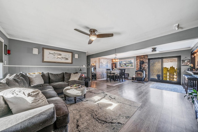 living room featuring wood-type flooring, a wood stove, ceiling fan, and crown molding