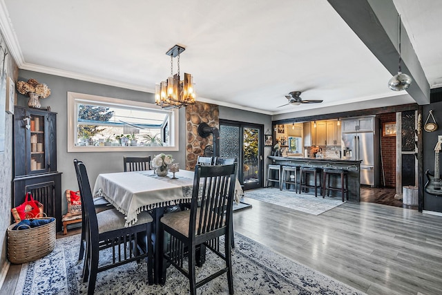 dining space with ornamental molding, dark wood-type flooring, and ceiling fan with notable chandelier