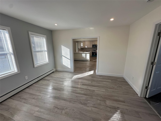 empty room with a baseboard heating unit, a wealth of natural light, and light hardwood / wood-style floors