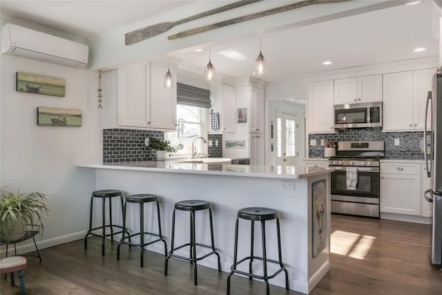 kitchen with appliances with stainless steel finishes, white cabinetry, a breakfast bar area, a wall mounted AC, and kitchen peninsula