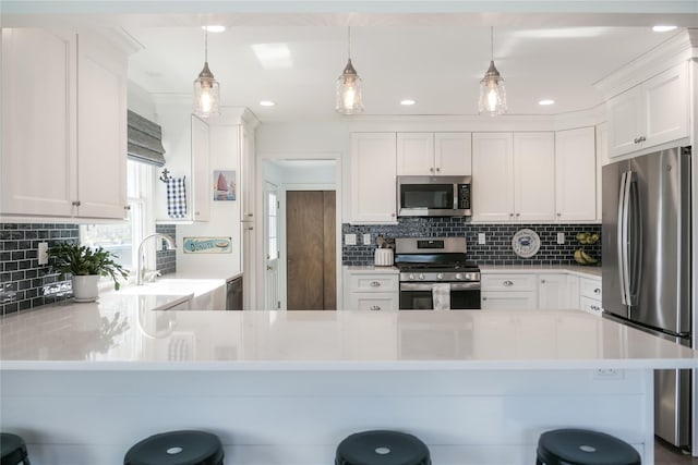 kitchen with pendant lighting, stainless steel appliances, a kitchen bar, and white cabinets