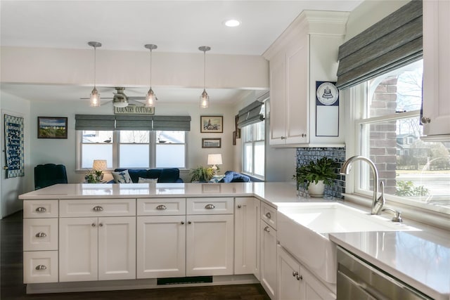 kitchen with decorative light fixtures, sink, white cabinets, stainless steel dishwasher, and kitchen peninsula