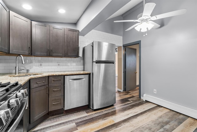 kitchen featuring sink, appliances with stainless steel finishes, a baseboard heating unit, tasteful backsplash, and light stone countertops