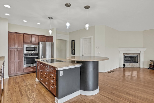 kitchen with light hardwood / wood-style flooring, hanging light fixtures, stainless steel appliances, light stone counters, and a fireplace