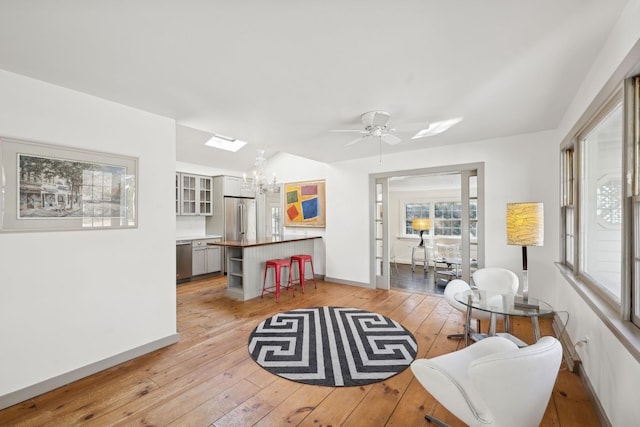 living room with ceiling fan with notable chandelier and light hardwood / wood-style flooring