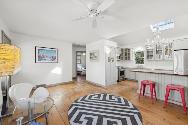 living room featuring ceiling fan with notable chandelier, a skylight, sink, and light wood-type flooring