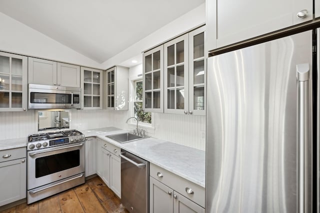 kitchen with sink, vaulted ceiling, appliances with stainless steel finishes, gray cabinets, and light stone countertops