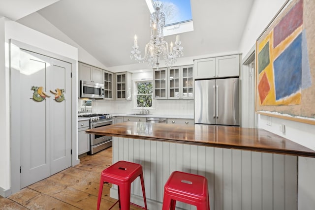 kitchen featuring sink, a breakfast bar area, stainless steel appliances, vaulted ceiling with skylight, and decorative light fixtures