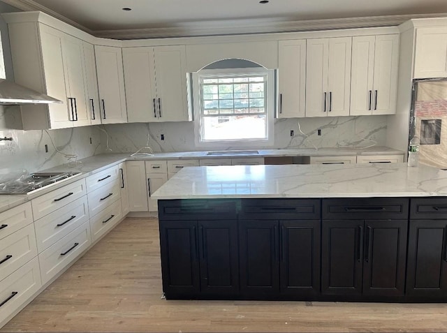 kitchen featuring wall chimney range hood, white cabinetry, dark cabinetry, and stovetop