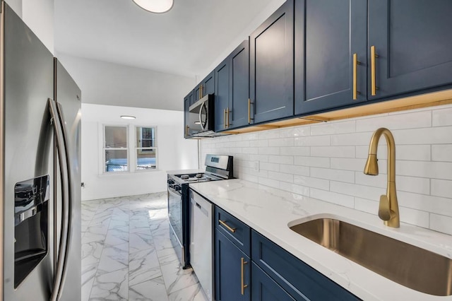 kitchen featuring blue cabinets, sink, light stone counters, stainless steel appliances, and backsplash