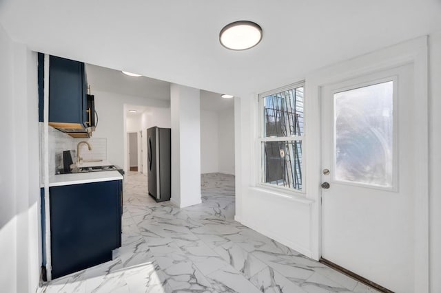 kitchen featuring blue cabinetry, sink, stainless steel fridge, and decorative backsplash