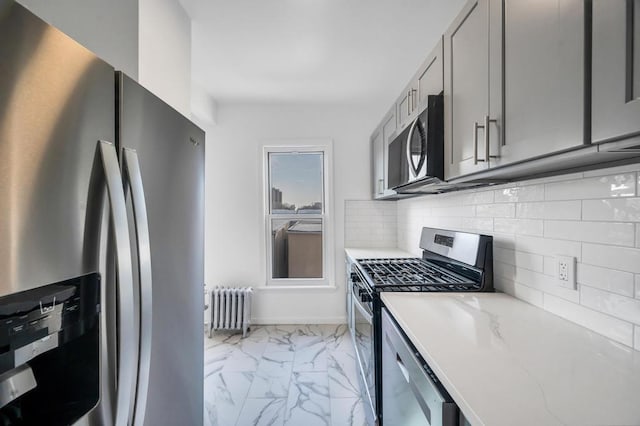 kitchen with gray cabinets, appliances with stainless steel finishes, radiator, tasteful backsplash, and light stone counters