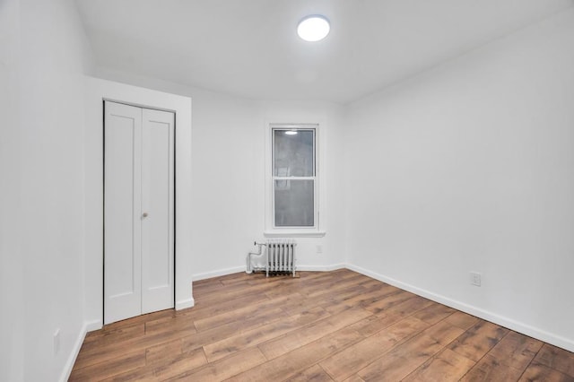 unfurnished bedroom with radiator, a closet, and light wood-type flooring