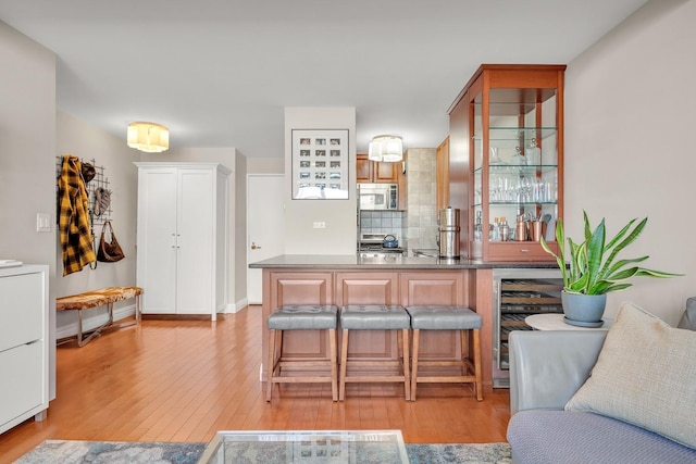 kitchen with wine cooler, a kitchen bar, tasteful backsplash, appliances with stainless steel finishes, and light hardwood / wood-style floors