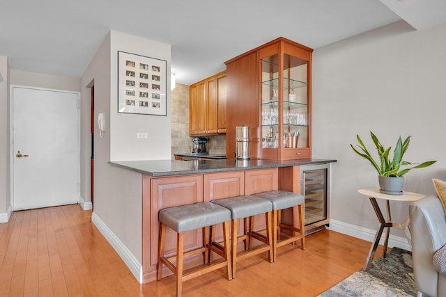 kitchen with a breakfast bar area, light wood-type flooring, kitchen peninsula, beverage cooler, and decorative backsplash