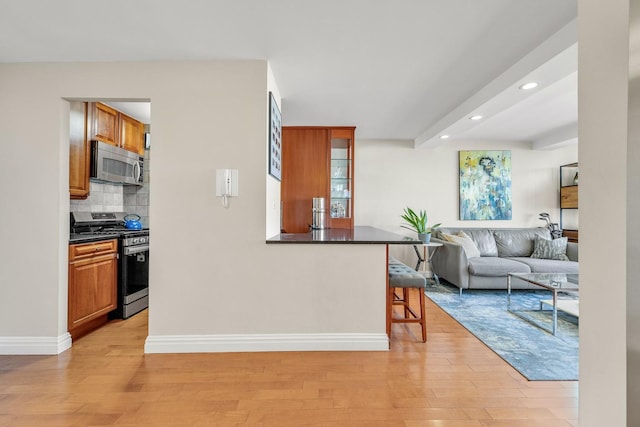 kitchen featuring a kitchen bar, backsplash, light wood-type flooring, and appliances with stainless steel finishes