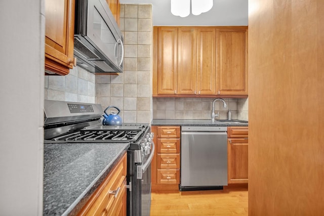 kitchen with sink, dark stone countertops, light wood-type flooring, appliances with stainless steel finishes, and decorative backsplash