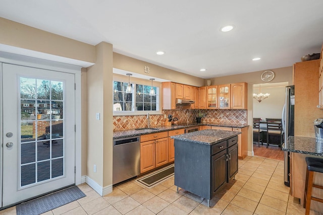 kitchen featuring sink, appliances with stainless steel finishes, a kitchen island, dark stone counters, and backsplash