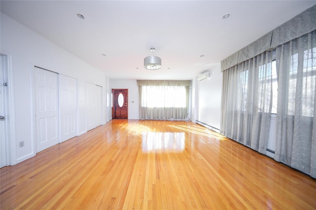 empty room featuring a baseboard heating unit, light wood-type flooring, and a wall unit AC