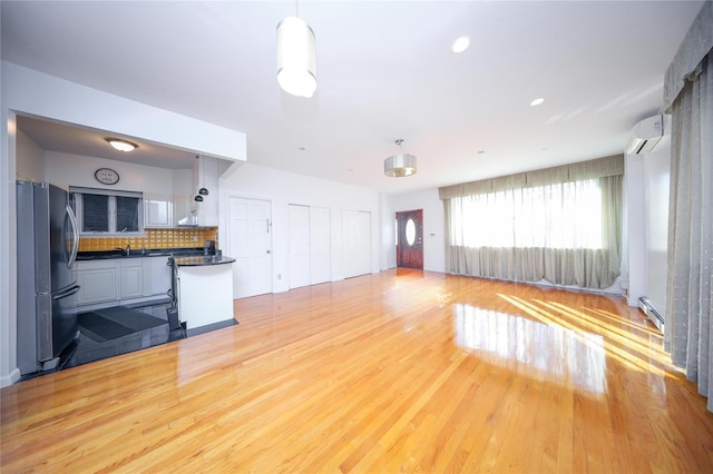 unfurnished living room with a baseboard heating unit, light hardwood / wood-style flooring, and an AC wall unit