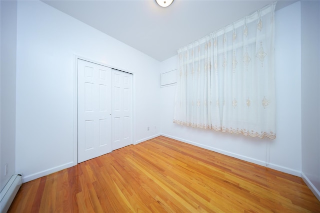 unfurnished bedroom with a baseboard radiator, hardwood / wood-style floors, and a closet