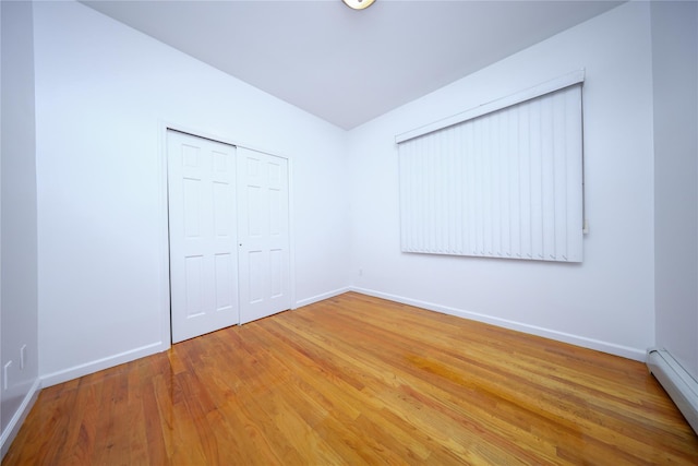 unfurnished bedroom featuring hardwood / wood-style flooring, baseboard heating, and a closet