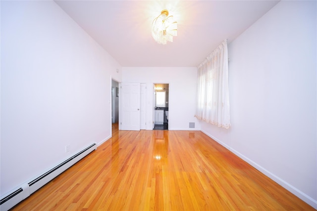 empty room featuring hardwood / wood-style flooring, a baseboard radiator, and an inviting chandelier