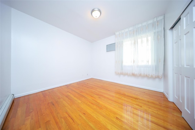 spare room featuring baseboard heating and light hardwood / wood-style flooring