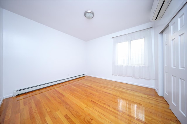 spare room featuring light hardwood / wood-style flooring, a baseboard radiator, and a wall unit AC