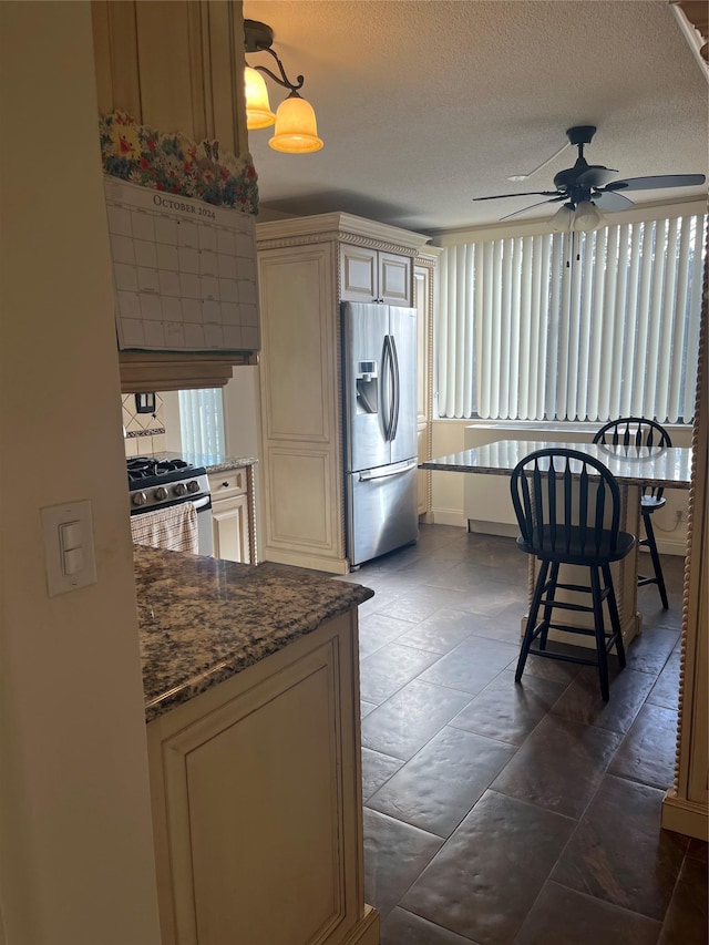 kitchen featuring dark stone countertops, hanging light fixtures, stainless steel appliances, cream cabinets, and a textured ceiling