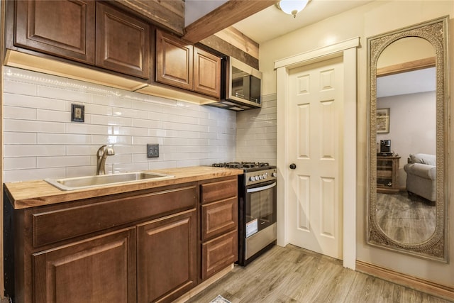 kitchen with stainless steel appliances, sink, light hardwood / wood-style flooring, and butcher block countertops