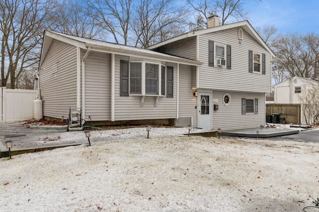 split level home featuring a chimney, fence, and cooling unit