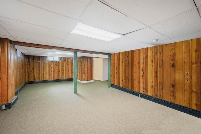 basement with carpet, a paneled ceiling, and wood walls