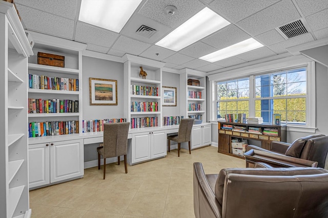 tiled office featuring a paneled ceiling, built in desk, and built in shelves