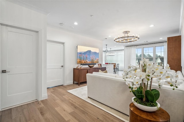 living room with an inviting chandelier, ornamental molding, and light wood-type flooring