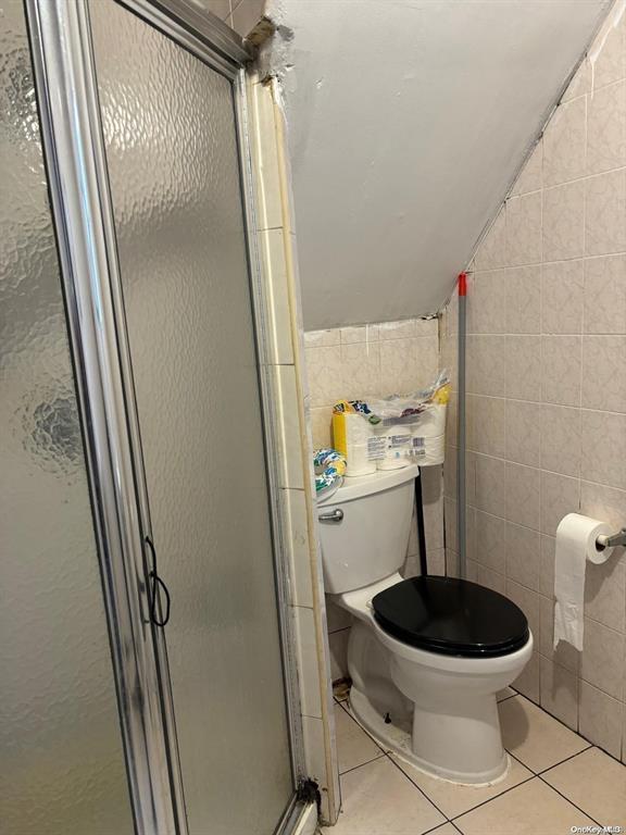 bathroom with an enclosed shower, vaulted ceiling, tile walls, and tile patterned floors