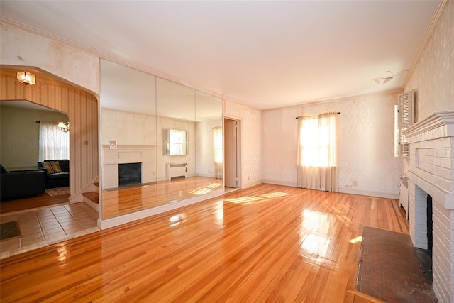 unfurnished living room with ornamental molding, radiator, light hardwood / wood-style floors, and a brick fireplace