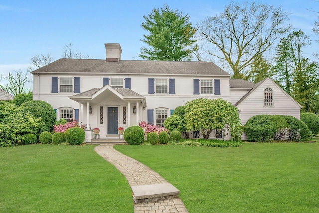 view of front of house featuring a front yard, roof with shingles, and a chimney