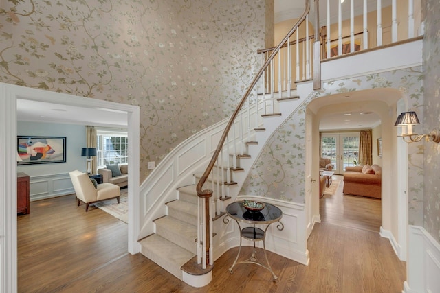 stairs with wallpapered walls, a wainscoted wall, ornamental molding, wood finished floors, and arched walkways