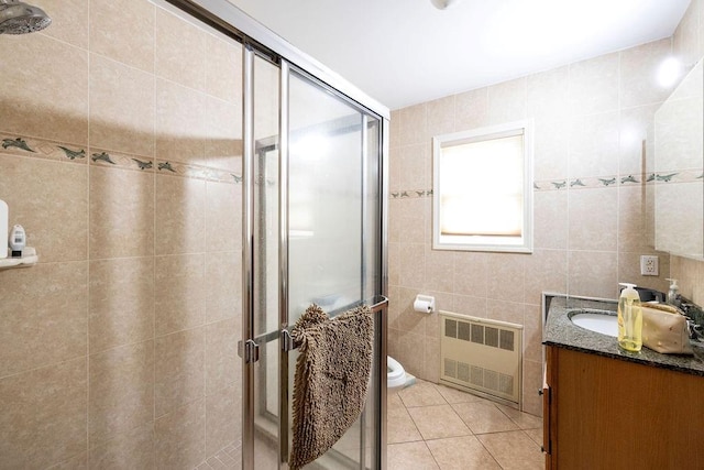 bathroom featuring a shower with door, tile walls, radiator heating unit, vanity, and tile patterned floors