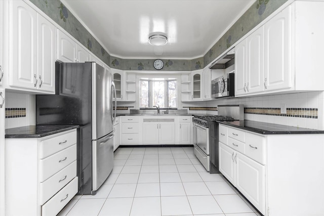 kitchen featuring sink, light tile patterned floors, stainless steel appliances, white cabinets, and dark stone counters