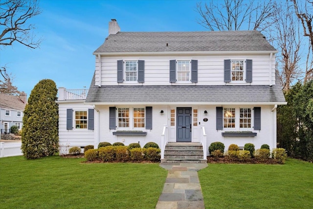 view of front of house featuring brick siding, a chimney, a front yard, and a shingled roof