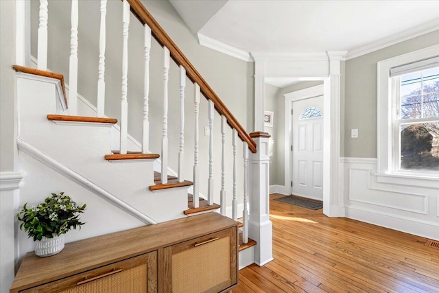 foyer featuring wainscoting, ornamental molding, light wood-type flooring, and a decorative wall