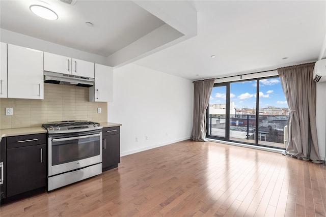 kitchen featuring light hardwood / wood-style flooring, white cabinetry, stainless steel gas range oven, expansive windows, and decorative backsplash