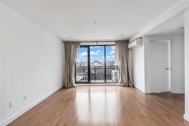 empty room with a wall mounted air conditioner, wood-type flooring, and floor to ceiling windows