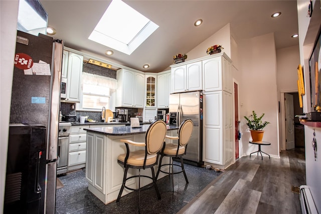 kitchen with appliances with stainless steel finishes, a skylight, a baseboard radiator, a breakfast bar area, and a center island