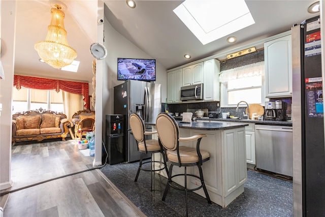 kitchen with a breakfast bar area, hanging light fixtures, appliances with stainless steel finishes, a kitchen island, and vaulted ceiling with skylight