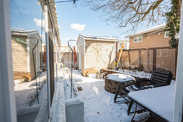 snow covered patio featuring an outdoor fire pit and a storage unit